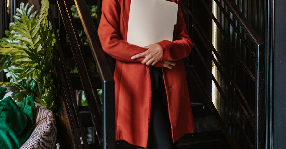 Smiling businesswoman in hijab holding a folder, standing on stairs in modern office.