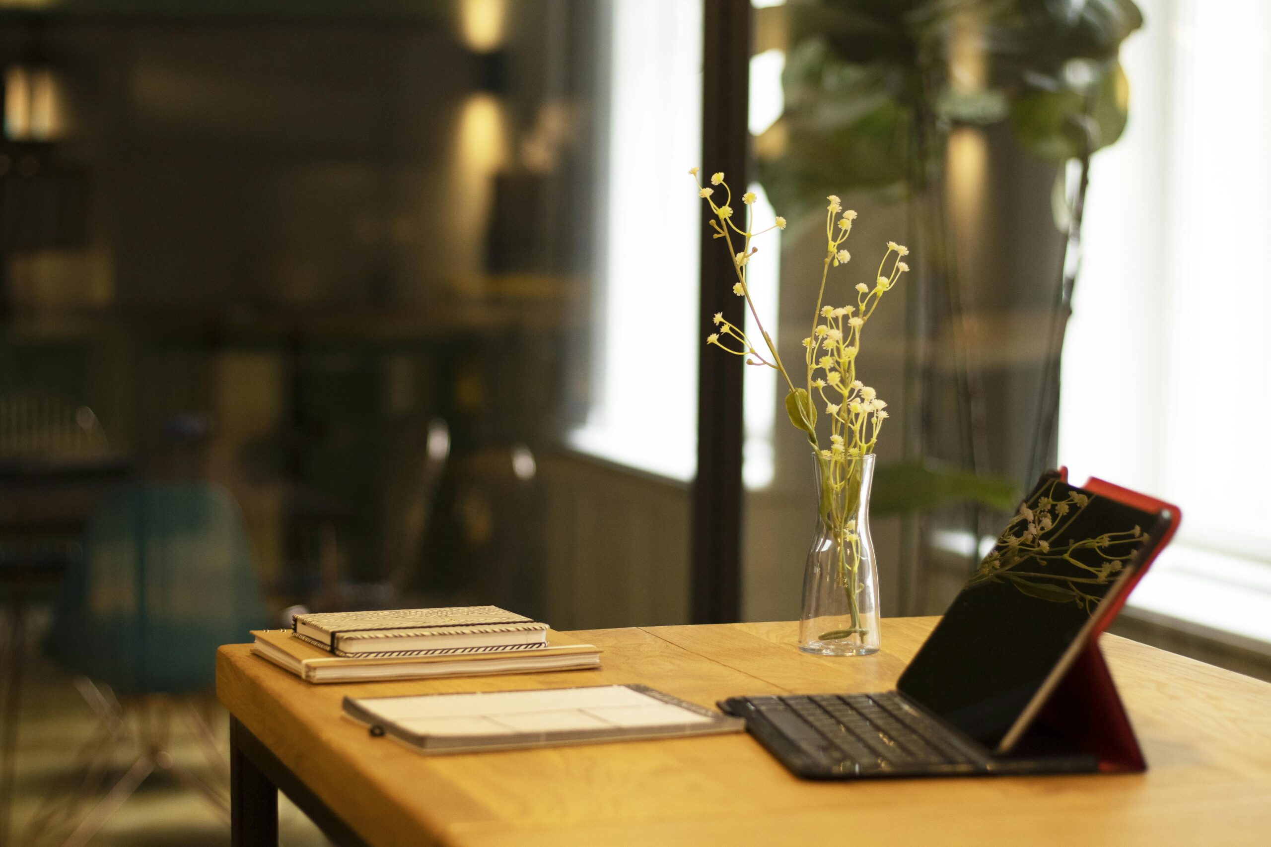 A serene indoor workspace featuring a tablet, books, and a vase on a wooden table.
